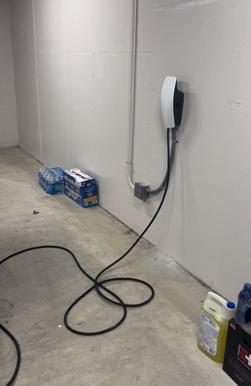 Electric vehicle charging station mounted on wall in a garage, with water bottles nearby.